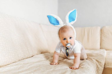 Tavşan kulaklı sevimli bebek evde kanepenin üzerinde paskalya yumurtalarıyla sepete doğru sürünüyor.