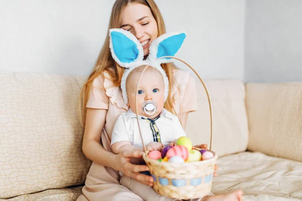 Mutlu Paskalyalar. Paskalya günü tavşan kulaklı bir anne ve küçük bir bebek, Paskalya yumurtası boyalı, eğlen, oyna ve sarıl, kanepede otur. Aile Paskalyayı kutluyor