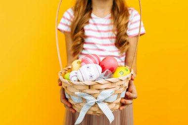 Tavşan kulaklı güzel, mutlu bir kız elinde sarı arka planda renkli yumurtalarla hasır bir sepet tutuyor. Paskalya ve baharın sembolü