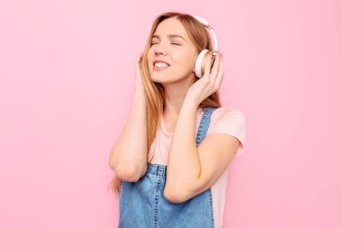 En sevdiği müziği büyük kulaklıklarla dinleyen genç bir kız, müziğin tadını çıkarırken, izole edilmiş pembe arka plana bakar.