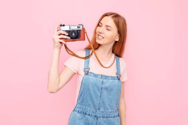 Çekici stil genç kız pembe arka planda izole edilmiş eski bir kamerayla fotoğraf çekiyor.