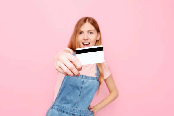 ピンクの背景に孤立したクレジットカードを持っているカジュアル服の幸せな若い女性の肖像画 — ストック写真