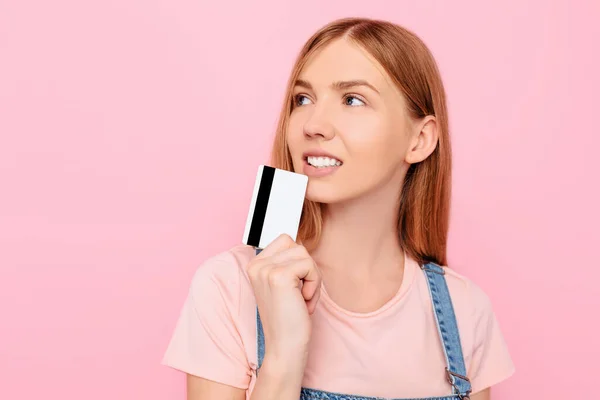 快乐的金发碧眼的年轻女人拿着信用卡 凝视着被粉色背景隔开的复制空间 — 图库照片