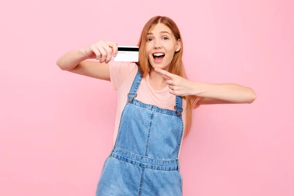 一个带着信用卡的惊喜交集的女人带着一张孤立的粉色背景的信用卡 — 图库照片