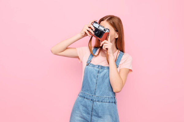 Attractive stylish young girl takes photos with a retro camera isolated on a pink background