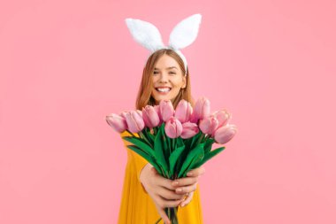 happy Easter. Happy attractive woman in Easter Bunny ears, girl with a bouquet of tulips, on an isolated pink background clipart