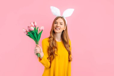 Mutlu Paskalyalar. Paskalya Tavşanı kulaklı mutlu çekici kadın, bir buket lalesi olan kız, izole pembe arka planda.