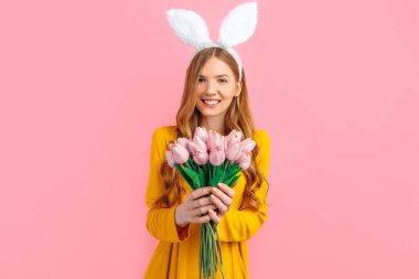 Mutlu Paskalyalar. Paskalya Tavşanı kulaklı mutlu çekici kadın, bir buket lalesi olan kız, izole pembe arka planda.