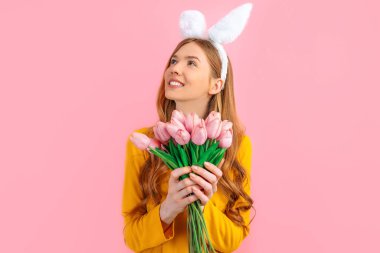 Mutlu Paskalyalar. Paskalya Tavşanı 'nın kulaklarında mutlu düşünceli bir kadın, bir buket lalesi olan bir kız, soyutlanmış pembe bir arka planda.