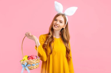 Mutlu Paskalyalar. Güzel, mutlu, genç bir kadın Paskalya gününde tavşan kulağı takar ve izole edilmiş pembe bir arka planda bir sepet yumurta tutar. Güzel kız Paskalya için hazırlanıyor.
