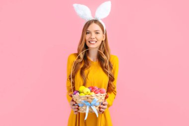Mutlu Paskalyalar. Güzel, mutlu, genç bir kadın Paskalya gününde tavşan kulağı takar ve izole edilmiş pembe bir arka planda bir sepet yumurta tutar. Güzel kız Paskalya için hazırlanıyor.