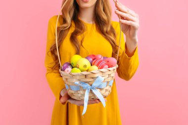 Eller, pembe arka planda renkli Paskalya yumurtalarının olduğu bir sepeti tutuyor. Mutlu Paskalyalar