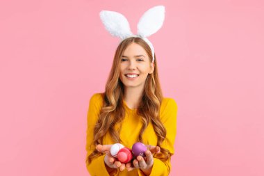 Mutlu Paskalya konsepti. Tavşan kulaklı mutlu bir genç kız pembe arka planda renkli Paskalya yumurtaları tutuyor..