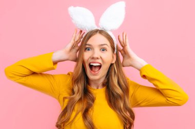 Shocked excited happy young woman in Easter Bunny ears isolated on pink background. clipart