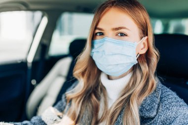 Maskeli güzel bir genç kız arabada oturuyor, Coronavirüs 'e karşı koruyucu maske takıyor, Coronavirus salgını sırasında şehir caddesinde şoför, covid-19.