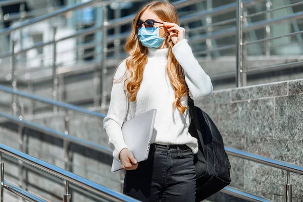 仕事から帰ってきた女性リモートワーク太陽の保護メガネを手にノートパソコンを手にしてコロノウイルスからのマスクの美しい若い女の子 — ストック写真