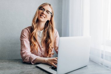 Odaklanmış genç bir kadın evinde oturuyor ve dizüstü bilgisayar kullanıyor. Uzaktan çalışma kavramı