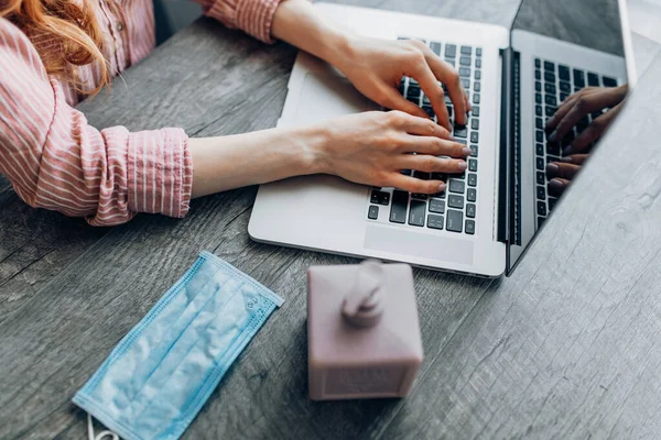 Close-up of a man disinfecting his hands with antiseptic while working at a computer, with a protective mask on the table. The concept of remote work in quarantine