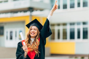 Yüksek lisans elbisesi içinde, elinde üniversiteden diploması olan mutlu, güzel bir kız öğrenci. Mezuniyet töreni konsepti