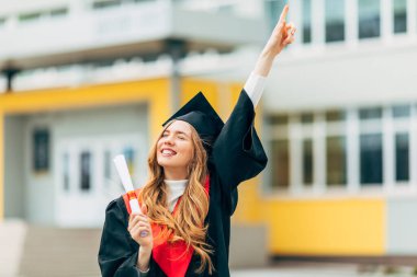 Yüksek lisans elbisesi içinde, elinde üniversiteden diploması olan mutlu, güzel bir kız öğrenci. Mezuniyet töreni konsepti