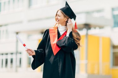 Yüksek lisans elbisesi içinde, elinde üniversiteden diploması olan mutlu, güzel bir kız öğrenci. Mezuniyet töreni konsepti