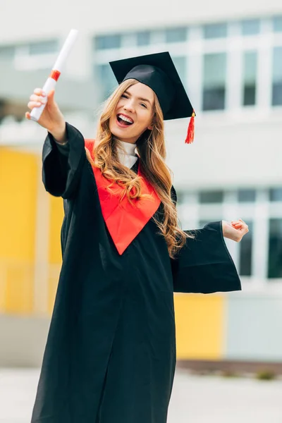 Happy beautiful girl student, in a master\'s dress, holding a diploma from the University. Concept of the graduation ceremony