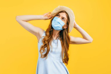 Yazın şapkalı bir kızın portresi, sarı izole edilmiş bir arka planda virüs enfeksiyonuna karşı tıbbi koruyucu bir maske takıyor. Karantina, koronavirüs, yaz