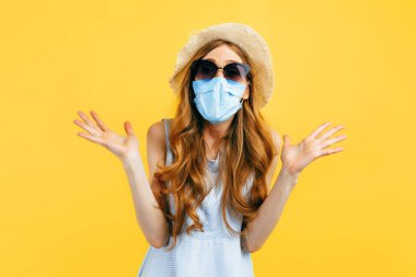 Yazlık şapkalı ve güneş gözlüklü mutlu bir kız sarı arka planda virüs enfeksiyonuna karşı koruyucu maske takıyor. Karantina, koronavirüs, yaz