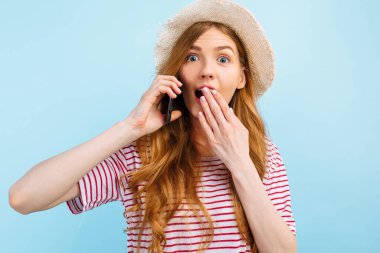 Yazlık şapkalı, ağzı kapalı konuşan, ağzı kapalı duran, mavi arka planda duran şaşırmış bir kız.