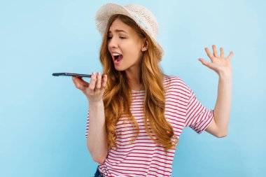 Sinirli agresif kız akıllı telefona bağırıyor, gergin bir şekilde bağırıyor ve telefonda konuşuyor, mavi arka planda izole edilmiş.