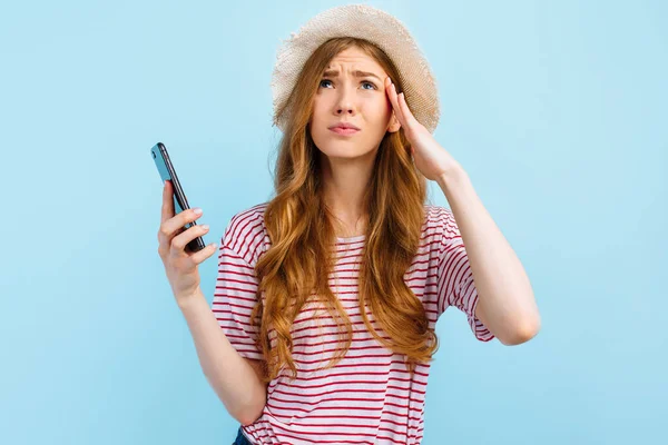 戴着夏帽的女孩 头疼难忍 用蓝色背景的手机 — 图库照片