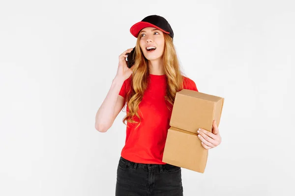 穿着制服 拿着纸板箱 拿着白色背景的手机聊天的年轻姑娘 网上购物 — 图库照片