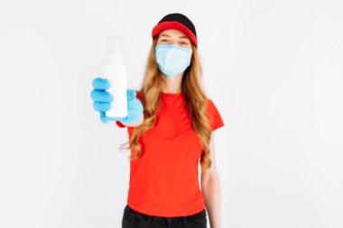 Üniformalı bir kurye, tıbbi lastik eldivenler ve maske, beyaz arka planda bir dezenfektan tutuyor. Hızlı teslimat. Çevrimiçi karantina ve koronavirüs
