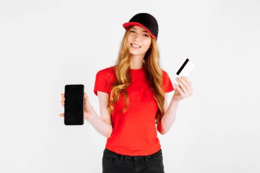 Üniformalı bir kurye kız, cep telefonu kullanıyor ve beyaz arka planda kredi kartı tutuyor. Teslimat, banka transferi ile ödeme,