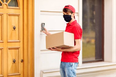 Elinde kutular olan koruyucu tıbbi maskeli bir kurye paketleri teslim eder. Karantina ve pandemik koronavirüs açısından servis teslimatı