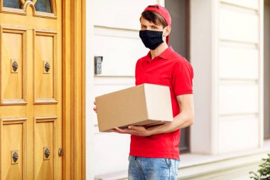 Elinde kutular olan koruyucu tıbbi maskeli bir kurye paketleri teslim eder. Karantina ve pandemik koronavirüs açısından servis teslimatı