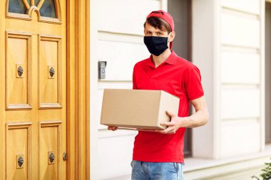 Elinde kutular olan koruyucu tıbbi maskeli bir kurye paketleri teslim eder. Karantina ve pandemik koronavirüs açısından servis teslimatı