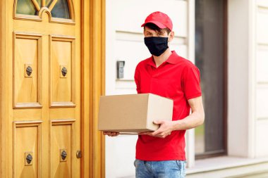 Elinde kutular olan koruyucu tıbbi maskeli bir kurye paketleri teslim eder. Karantina ve pandemik koronavirüs açısından servis teslimatı
