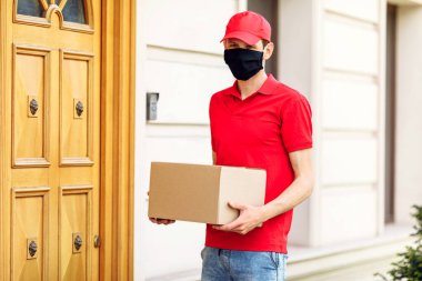 Elinde kutular olan koruyucu tıbbi maskeli bir kurye paketleri teslim eder. Karantina ve pandemik koronavirüs açısından servis teslimatı