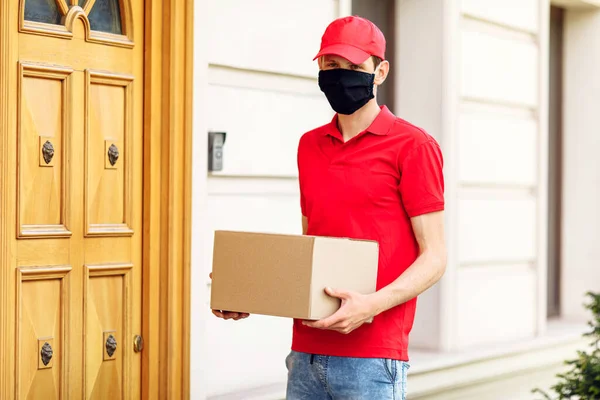 A courier in a protective medical mask with boxes in his hands delivers parcels. Service delivery in terms of quarantine, pandemic coronavirus