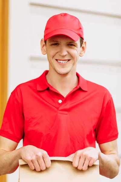 Een Koerier Een Rood Uniform Heeft Een Papieren Zak Met — Stockfoto