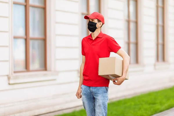 A courier in a protective medical mask with boxes in his hands delivers parcels. Service delivery in terms of quarantine, pandemic coronavirus