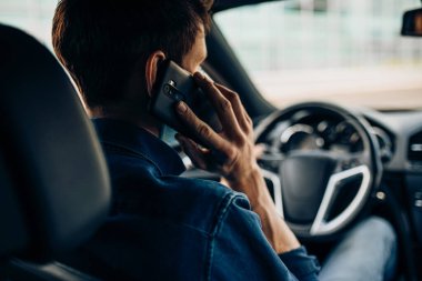 Araba kullanırken direksiyonu tutan ve cep telefonuyla konuşan bir adamın yakın çekimi.