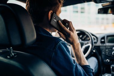 Araba kullanırken direksiyonu tutan ve cep telefonuyla konuşan bir adamın yakın çekimi.