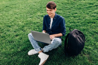 Parktaki çimlerin üzerinde dizüstü bilgisayarla oturan güzel bir öğrencinin portresi.