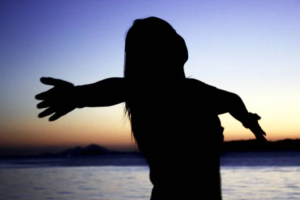 Siluate meisje op het strand bij zonsondergang. — Stockfoto