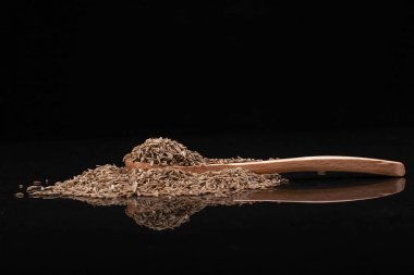 Kimyon tohum tahta kaşıkla siyah arka plan üzerinde