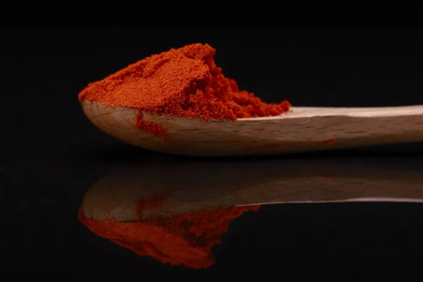 Chili Powder  over Black background with wooden spoon