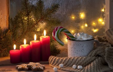 close-up of hot mug with marshmallow and candy canes with red candles, Christmas decor on festive background. Christmas concept.  