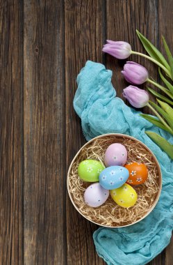 renkli yumurta yuvada ahşap masa mavi eşarp ve lale çiçekleri ile yakın çekim.